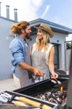 Happy couple enjoying a sunny summer day, grilling marshmallows on a rooftop barbecue, sharing