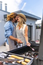 Romantic couple sharing a kiss while grilling marshmallows during a barbecue on a rooftop terrace