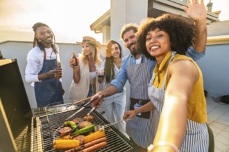 Cheerful multi ethnic friends are grilling meat and vegetables, drinking beer and taking a selfie