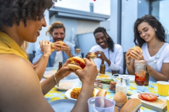 Cheerful multi ethnic friends savoring delicious burgers while enjoying a lively rooftop barbecue
