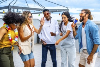 Group of cheerful multi ethnic friends having fun singing karaoke and dancing together at a rooftop