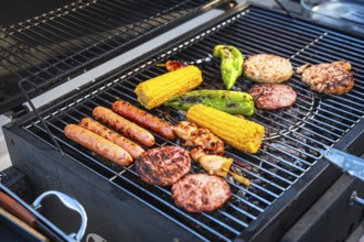 Sizzling sausages, juicy hamburger patties, tender chicken, and sweet corn cobs grilling over a