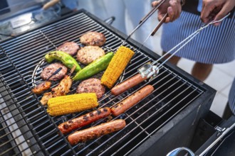 Chefs grilling several hot dogs, hamburgers, corn and peppers on a hot grill for a summer barbecue