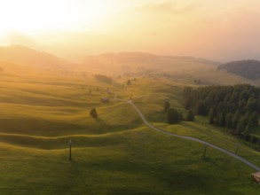 Soft hills and meadows in the golden light of sunset with scattered mountain huts, Alpe di Siusi,