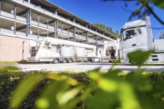 Lorry and trailer in front of a modern building, surrounded by green leaves in the foreground,