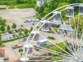 Ferris wheel with visible cabins, parked cars and green surroundings, construction of Ferris wheel,