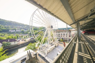 A Ferris wheel stands next to a river under the roof of a multi-storey car park, surrounded by