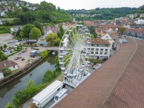 Aerial view of a Ferris wheel in the middle of a town in summer weather and wooded surroundings,