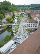 A large Ferris wheel towers over the city centre, surrounded by the river and green landscape,