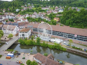 A Ferris wheel next to a river in the centre of a town with a green hilly landscape in the