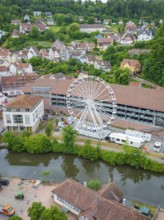 A large Ferris wheel stands in an urban environment near a river and surrounded by residential