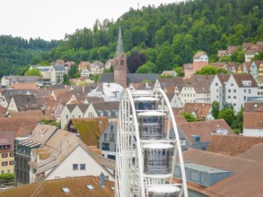 Ferris wheel in the foreground of a town view with church and wooded hills, Ferris wheel