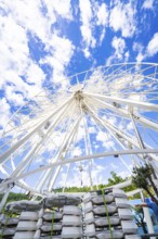 Partially erected Ferris wheel in front of a clear blue sky with cloud formations, Ferris wheel