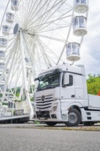 Large Ferris wheel in the background of a parked white lorry on a cloudy day, Ferris wheel