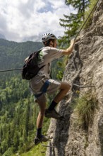 Mountaineer climbing over a steep ladder in the Isidor via ferrata, Grünstein, Schönau am