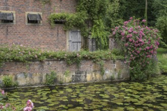 Romantic garden with brick wall, roses and water lilies in the calm water, Haus Welbergen,