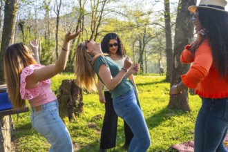 Four friends enjoying a sunny day in the park, dancing and listening to music from a portable