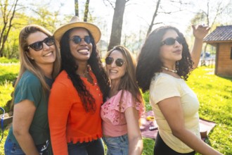 Four diverse women wearing stylish sunglasses and sharing joyful smiles while relaxing together in