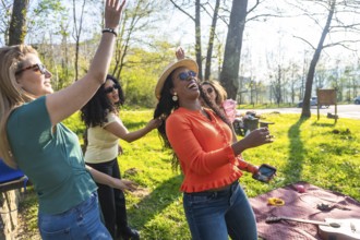 Four women dancing and enjoying themselves during a picnic in a park, celebrating friendship and