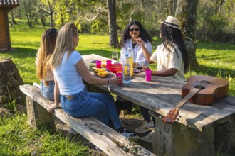 Four young women are having a picnic on a wooden table, with wine, fruit, and a guitar, enjoying