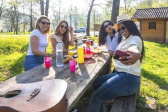 Four young women taking a selfie with smartphone at a picnic table in a park during a sunny day,