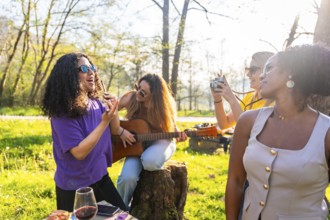 Four young women enjoying a picnic in a park, singing, playing guitar, taking pictures, and having