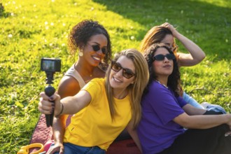 Four cheerful female friends are recording a video blog in the park using an action camera,