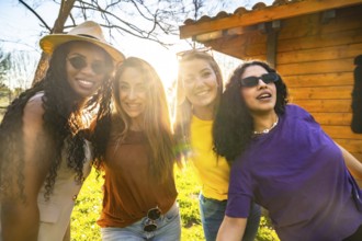 Four diverse young women are smiling and embracing outdoors, enjoying the warm glow of sunset light