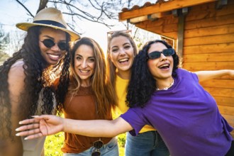 Four multi ethnic female friends are enjoying a sunny day in a garden, smiling and embracing each