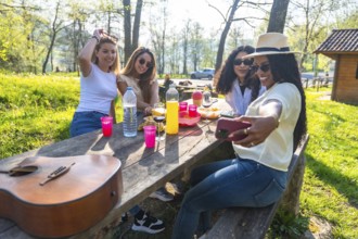 Four diverse young women taking a selfie while enjoying a picnic in a park, capturing memories of