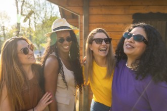 Four multi ethnic female friends are enjoying a sunny day together, laughing and embracing outdoors