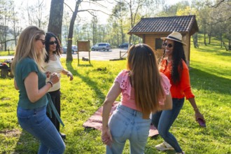 Four beautiful multi ethnic women dancing and having fun at a picnic in a park during a sunny day