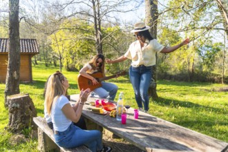 Happy friends are having a picnic in nature, playing guitar, dancing, and enjoying good company