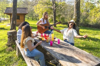 Four young women enjoying a sunny day at the park, playing music, eating fruit, and having fun