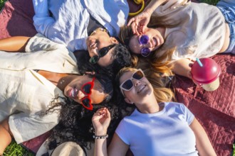 Four diverse female friends are relaxing on a blanket in a park, enjoying a sunny day together