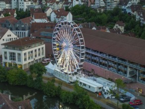 Illuminated Ferris wheel on an evening, surrounded by buildings and water, 950 years of Calw,