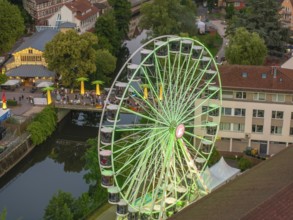 A green Ferris wheel stands near a bridge and a river, surrounded by trees, 950 years Calw, Germany