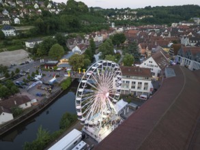 Urban landscape with a Ferris wheel at dusk next to a river, 950 years of Calw, Germany