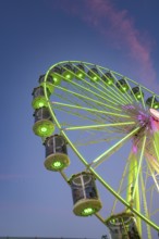 An illuminated Ferris wheel with green-red light is reflected in a river at dusk, 950 years Calw,