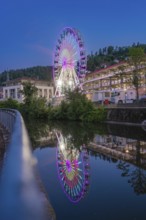 A large white Ferris wheel in front of a mountainous landscape and bright daylight, surrounded by