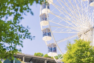 Close-up of a Ferris wheel with cabins, visible between green trees and a blue sky, 950 years Calw,