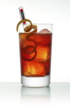 Campari cocktail in a long drink glass on ice with orange zest as garnish against a white