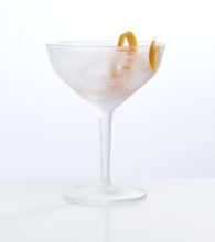 Frosted empty cocktail glass with orange zest as garnish against a white background, studio shot