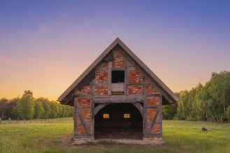 View of an open half-timbered barn standing on a pasture in the sunset, meadow, spring, awakening,