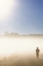 Man running on a dirt road in morning fog in the countryside with the sun shining through the fog