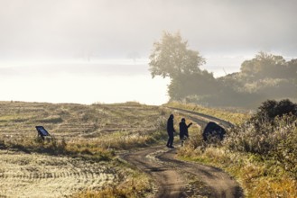 Couple standing on a winding gravel road in a rolling agricultural landscape with low morning mist
