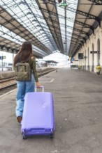 Tourist walking along a train platform, pulling a trolley suitcase while embarking on an exciting