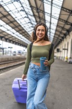 Tourist walking in train station pulling suitcase and listening to music with headphones, holding