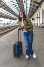Tourist using a smartphone while waiting for the train at the railway station, enjoying the journey