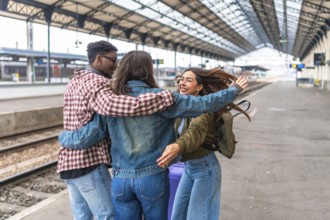 Three happy multi ethnic young adult students hug at train station after arriving for a trip